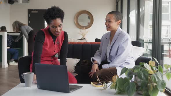 Slow motion of mixed race LGBTQ mid adult woman and mature black woman using laptop in office