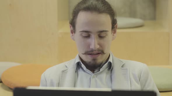 Close-up Portrait of Young Caucasian Man with Mustaches and Beard Looking at Laptop. Positive alt