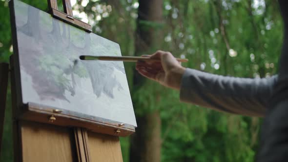 Girl with a Brush in Her Hands Paints a Lake and Trees on Canvas. alt