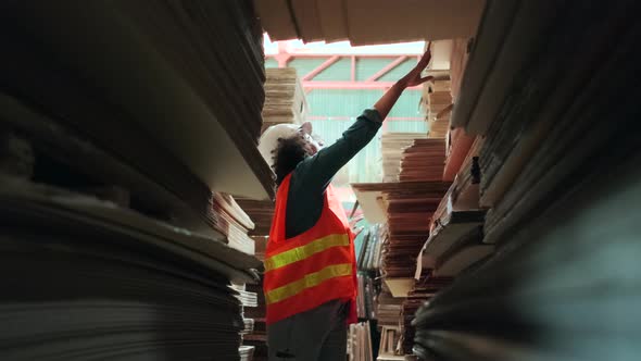 African American female worker inspects stock order at paper factory warehouse. alt
