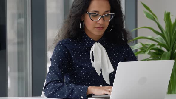 Young professional mixed race female using computer sitting at office desk. Focused business woman e
