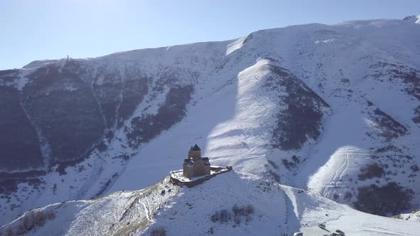 Aerial footage of lonely old medieval Gergeti Trinity Church in winter mountains in Kazbegi Georgia