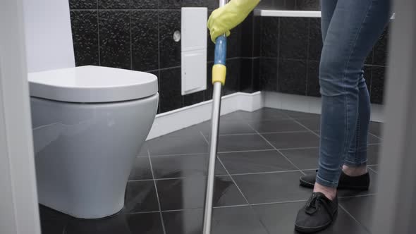 A cleaning lady in yellow gloves washes the floor in the toilet. House cleaning.