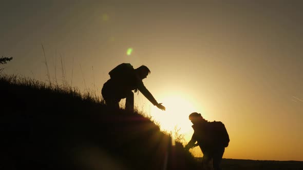 Traveler Man Extends His Hand To a Girl Climbing To the Top of a Hill. Travelers Climb the Cliff alt