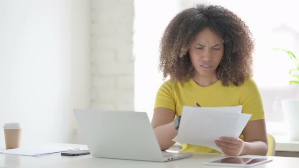 African Woman with Laptop Having Loss while Reading Documents alt