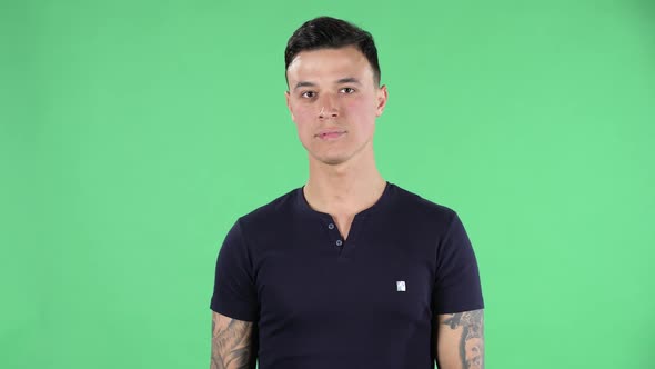 Portrait of a Handsome Young Guy Looking Straight Smiling and Showing a Heart Gesture and Air alt