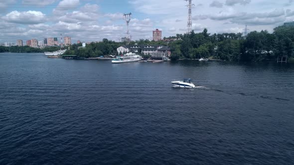 Aerial View of Motorboat Sailing Over Te Waves on the River Against the Background of Harbor with