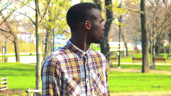 A Young Black Man Waits for Someone in a Park on a Sunny Day alt