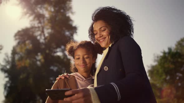 Happy Mother Holding Smartphone Making Selfie with Cute Daughter in Spring Park alt