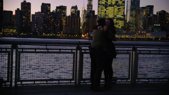Couple in New York City standing on pier at night with city skyline in background