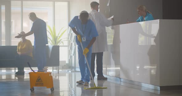 Afroamerican Janitor in Headphones Washing Floor in Hospital Reception Area