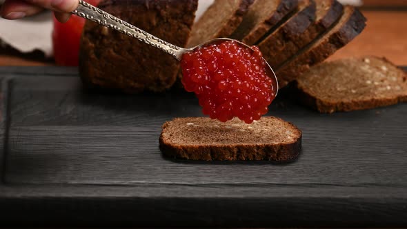 red caviar spills out of a spoon on a piece of rye bread alt