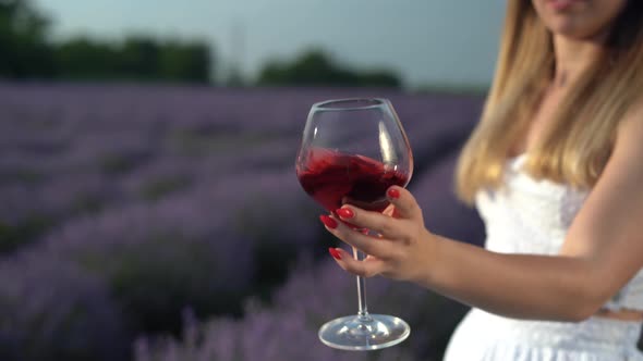 Closeup of a Girl's Hand with a Glass of Red Wine on the Background of a Lavender Field alt