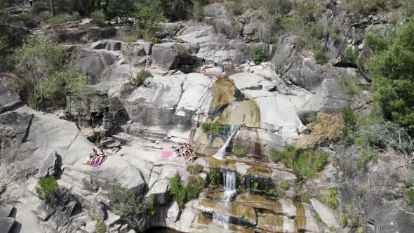 Aerial top down over people sunbathing above rocks, at waterfall Fecha de Barjas. Geres, Portugal
