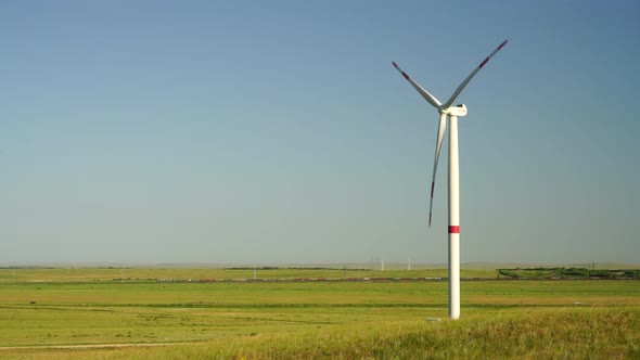 Motion the Blades of a Large Wind Turbine in a Field Against a Background of Cloudy Blue Sky with alt