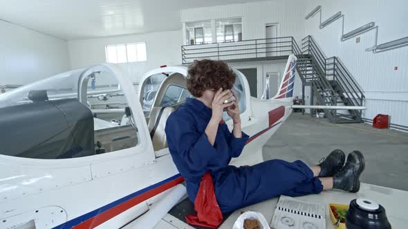 Female Aircraft Mechanic Drinking Tea while Having Lunch in Hangar alt