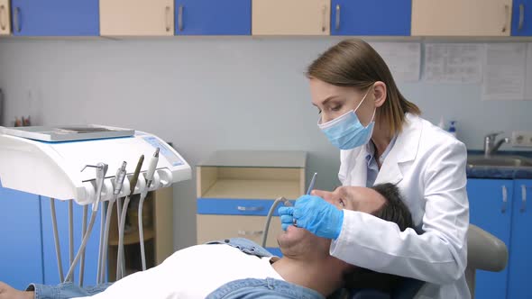 Dentist in Mask Treating Cavity of Patient's Teeth alt