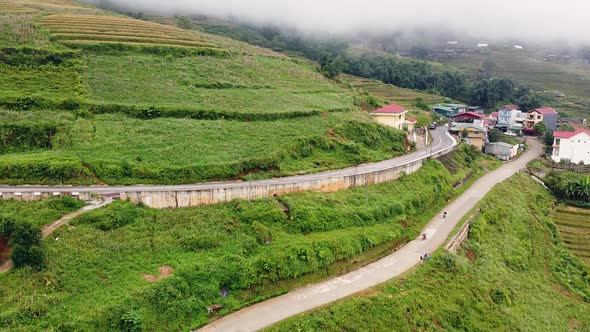 Aerial View of a Curvy Road, Small Village, and Rice Terraces in the Mountains. alt
