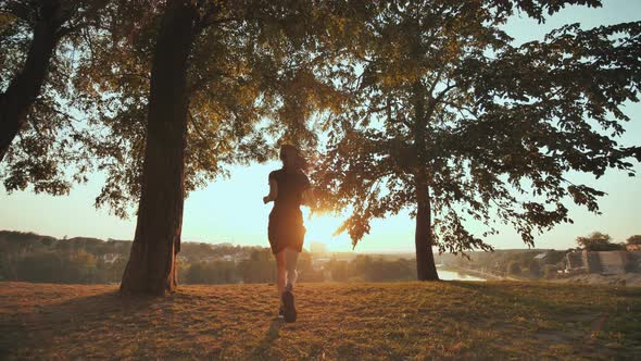 The Girl Enthusiastically Runs to Meet the Sunset on the Background of the City and Raises Her Hands alt