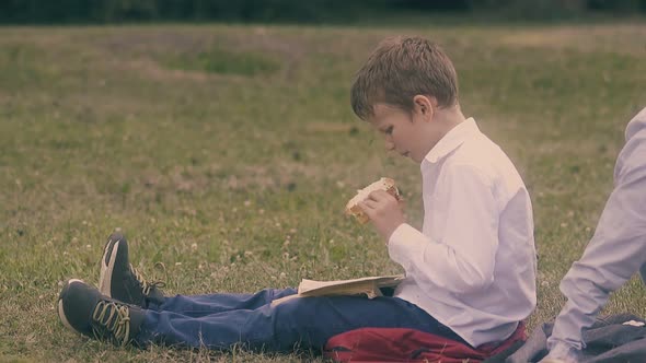 Boy in White Shirt Sits on Grass and Eats Tasteless Sandwich alt