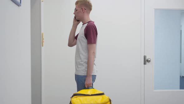 Side View Portrait of Young Caucasian Man Talking on Phone Waiting for Lift with Yellow Food alt