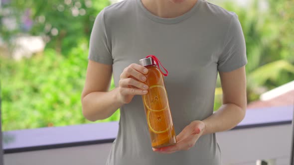 A Woman Holds a Bottle of Kombucha Drink in Her Hands Which Has an Orange Flavor alt