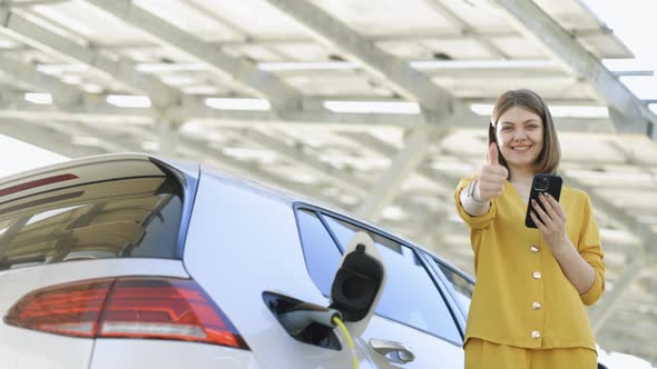 Businesswoman Standing on Charging Station Looking at Camera and Showing Thumb Up