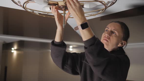 Woman Doing Electrical Maintenance and Replacing the Lamp on the Chandelier alt