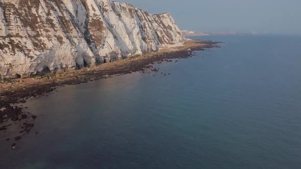 Drone flies low towards the White Cliffs of Dover with camera panning up. Beautiful turquoise sea in alt