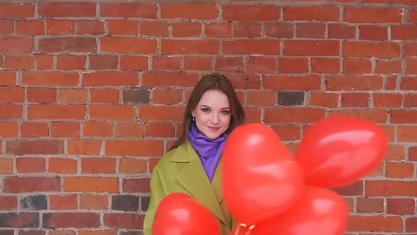 Portrait of an Elegant Young Woman with Red Balloons Against a Red Brick Wall on the Street alt