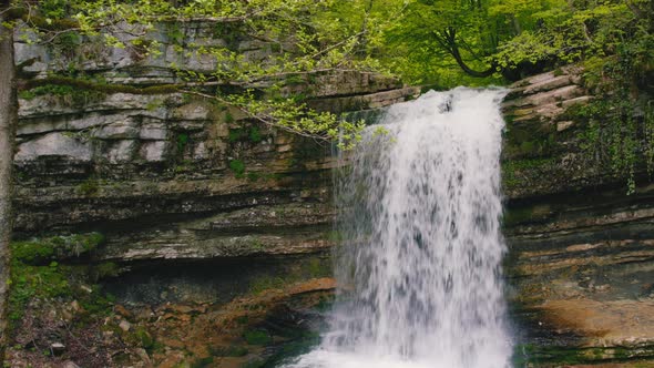 Scenic Drone Shot of a Small Fresh and Fast Cascade in the Forest Spring Green Vegetation Aerial alt