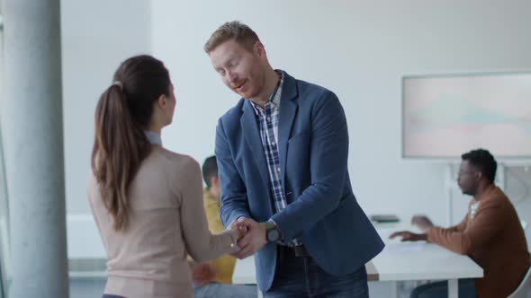 Young business partners making handshake in an office while their team working in the background