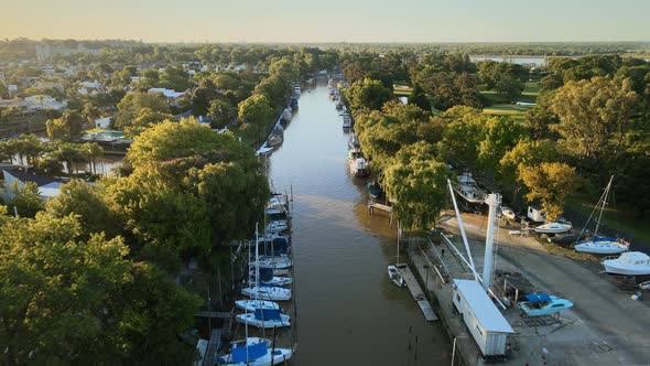 Aerial following a river path with several boats docked and at sides some houses. Dolly in alt