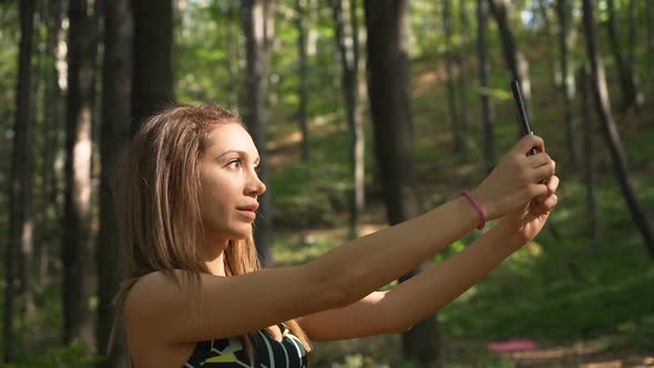 Beautiful Fit Girl in Sportswear Fixing Her Hair and Taking Selfie Picture with Mobile Phone alt