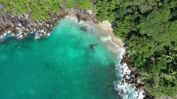 Aerial view of waves crashing into secret cove, sea and forest Mahe Seychelles