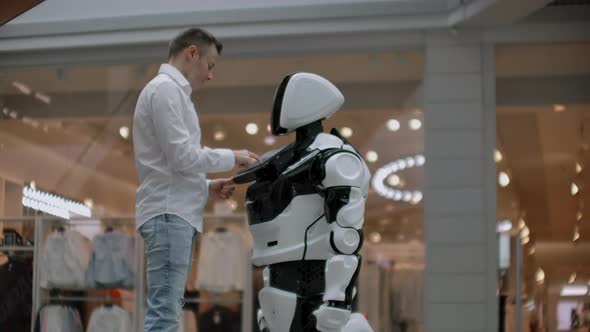 A Man in a Shirt Communicates with a White Robot Asking Questions and Pressing the Screen with His alt
