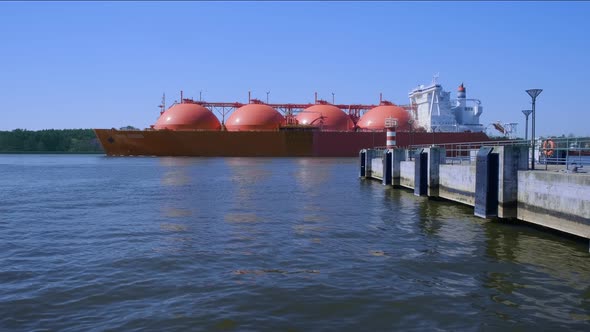 Liquified natural gas tanker or LNG carrier ship pass by wharf to enter industrial port on sunny day