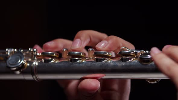 Female hands of musician hold flute and play melody with fingers, studio dark background, slide. alt