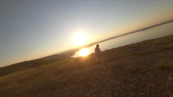 Panoramic Aerial Shot From Fpv Drone of Happy Young Woman on Top of Hill Watching Sunset Near Lake alt
