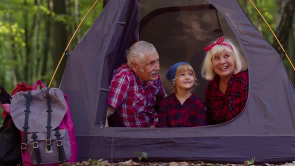 Senior Grandmother Grandfather with Granddaughter Sitting in Tourist Tent Over Campfire in Wood alt
