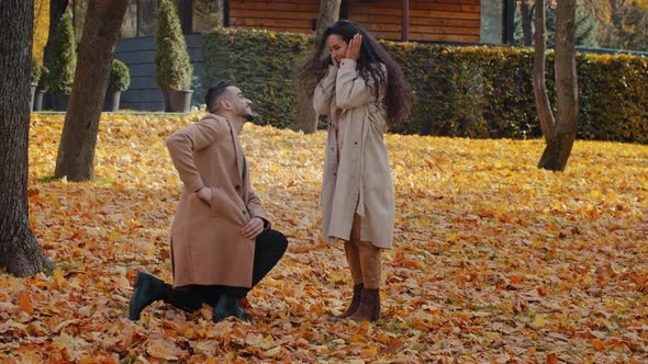Hispanic Loving Couple in Autumn Park Man Stand in Yellow Leaves on One Knee Making Marriage alt