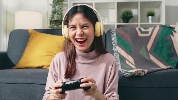 woman sitting on sofa with wearing headphones and holding joystick with playing games.
