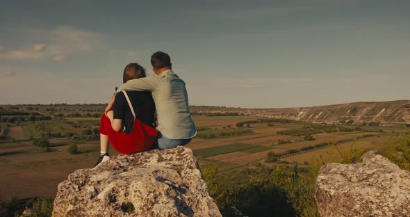 Young Couple Hugging While Sitting on A Cliff with A Beautiful View