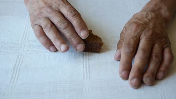 Close-up shot of an elderly man taking a piece of bread from the table. alt
