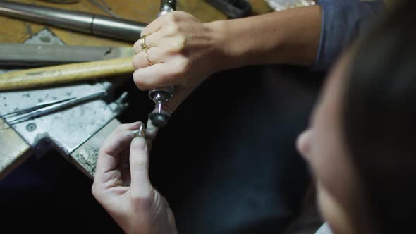 Close up of hands of caucasian female jeweller using tools, making jewelry alt