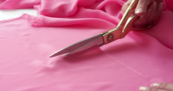Beautiful Close View of Female Hand Cutting Pink Fabric with Scissors alt