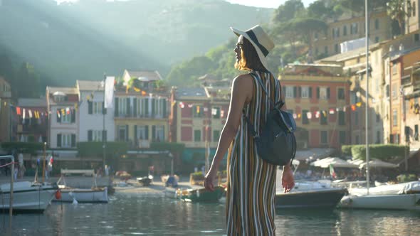 A woman walking wearing hat and backpack purse traveling, Portofino, Italy, luxury resort, Europe alt