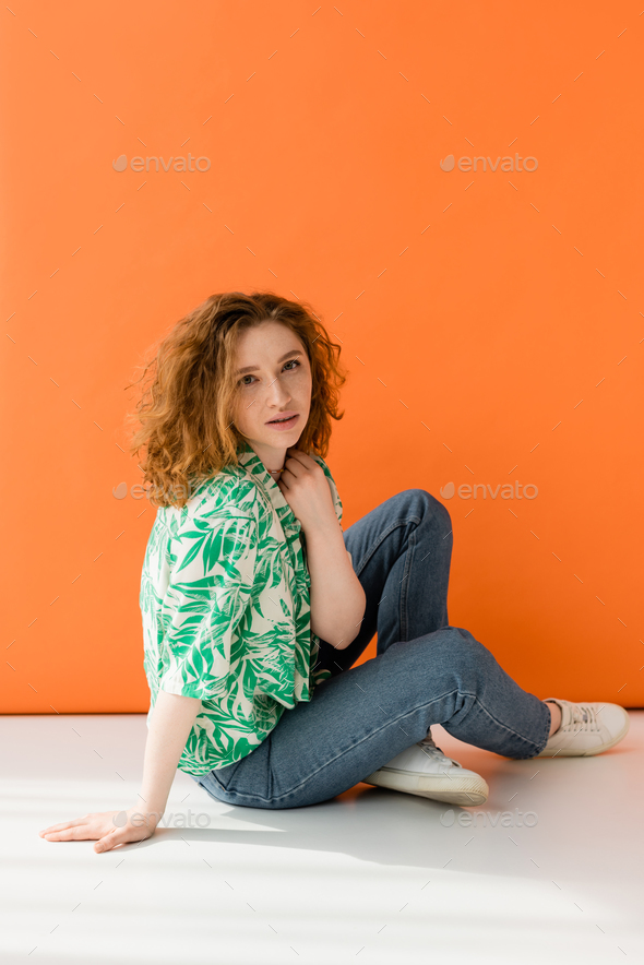 Young red haired model in modern blouse with floral pattern and jeans