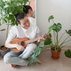 young woman at home playing ukulele sitting near green plants - PhotoDune Item for Sale