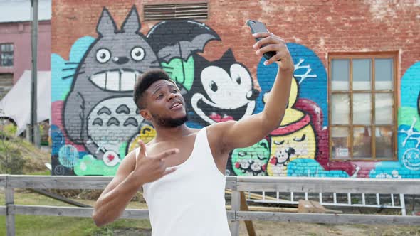 Young Black Guy With Mobile Phone In His Hands. He On Graffiti Wall Background. alt